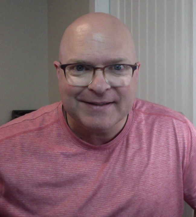 Joseph Trevors smiling in a casual dark pink t-shirt, offering a warm and approachable presence.