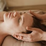 A woman receiving a relaxing facial reflexology therapy, with gentle hands massaging her temples, symbolizing the therapeutic benefits of Carol Earle's services.