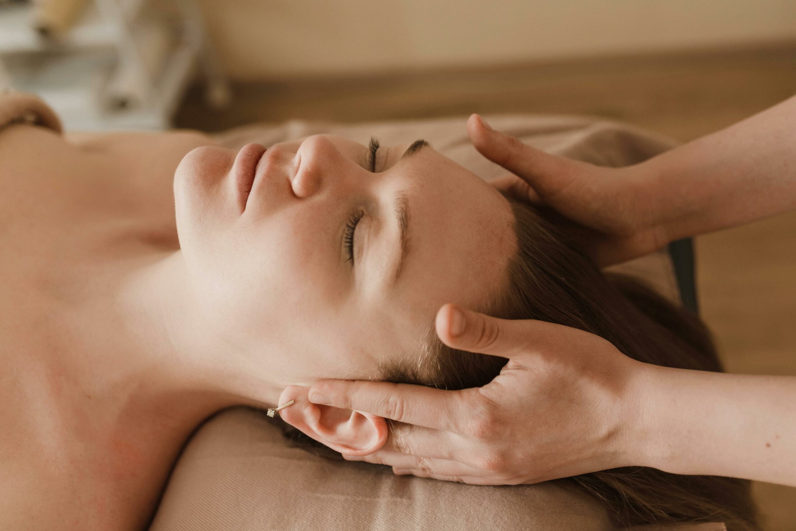 A woman receiving a relaxing facial reflexology therapy, with gentle hands massaging her temples, symbolizing the therapeutic benefits of Carol Earle's services.