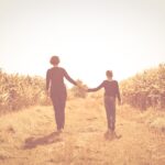 A mother and child walk hand-in-hand down a rural path, symbolizing the connection between childhood upbringing and adult behavior.