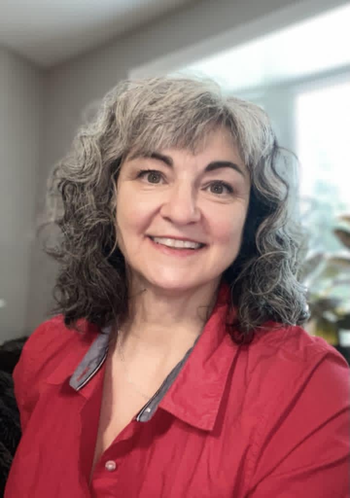 Marie-Élaine Beaulieu, a smiling woman with curly salt-and-pepper hair, wearing a red blouse, seated in a naturally lit room.